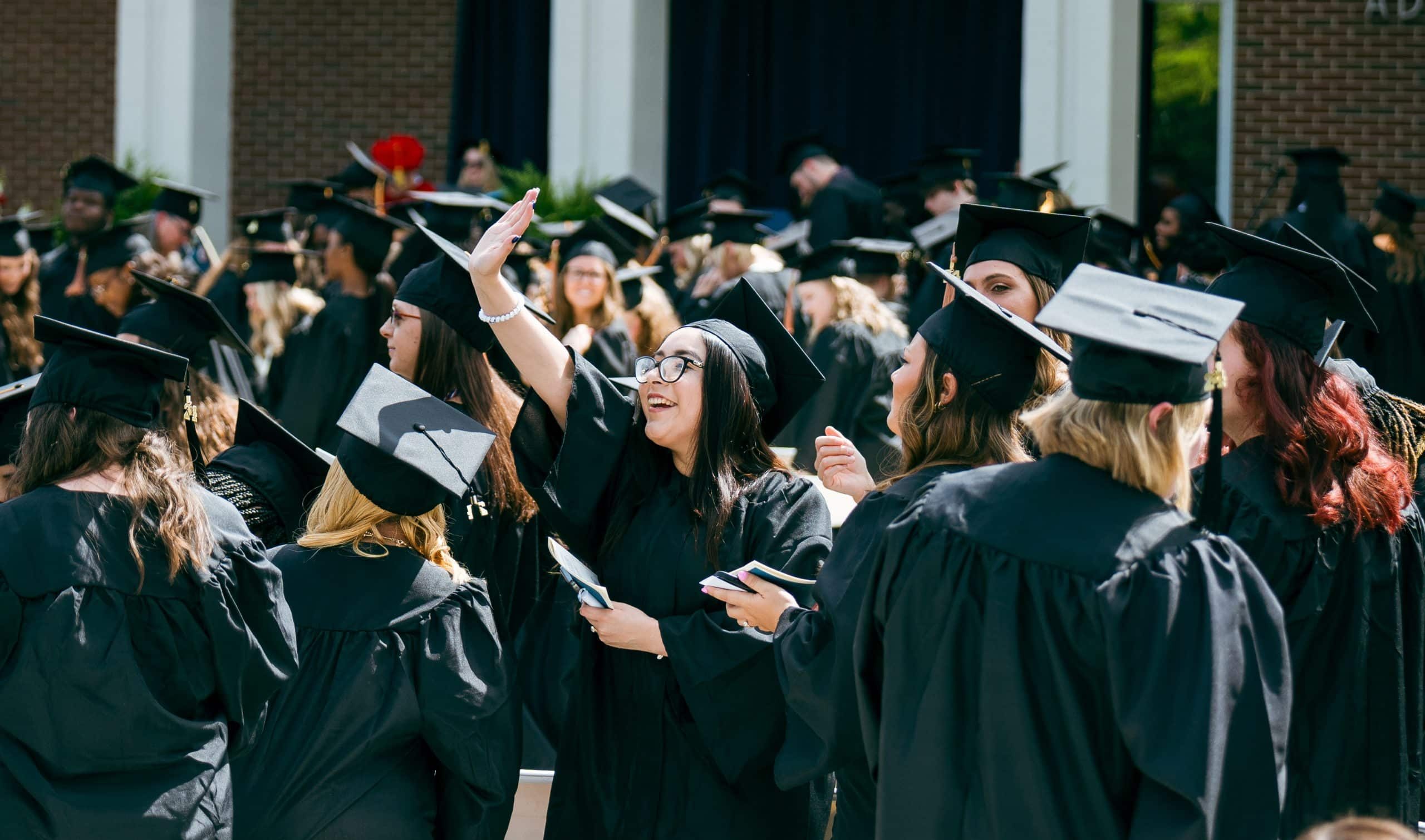 Student waving in a crowd during DSCC Commencement.